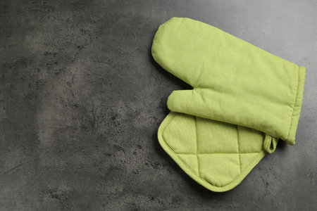 Green oven glove and potholder on dark textured table, top view. Space for textの写真素材