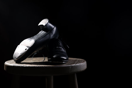 Pair of shoes for tap dance on wooden stool against black background, closeup. Space for textの写真素材