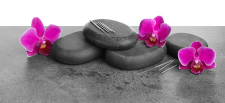 Acupuncture needles, orchid flowers and spa stones on grey textured table against white background, closeupの写真素材