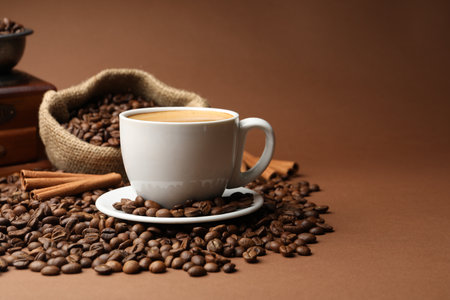 Cup of hot coffee, beans, grinder and cinnamon on brown background, closeupの写真素材