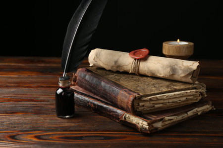 Old rolled scroll, burning candle, feather, inkwell and books on wooden table, closeup