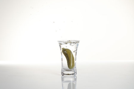 Vodka with pickle in shot glass isolated on whiteの写真素材