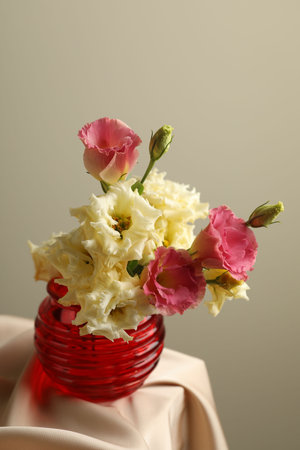 Beautiful flowers in glass vase on beige cloth against light background, closeupの写真素材