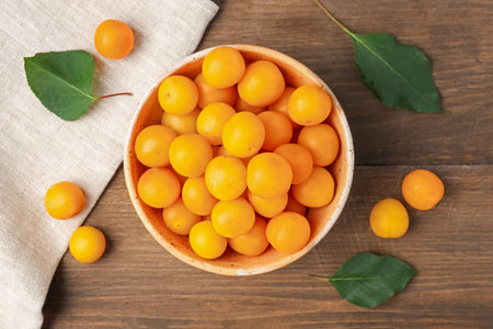 Ripe yellow cherry plums and leaves on wooden table, flat layの写真素材