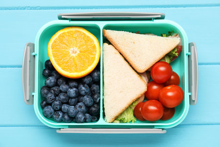 Open lunch box with tasty food on light blue wooden table, top view