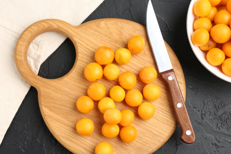 Ripe yellow cherry plums, wooden board and knife on black table, flat layの写真素材