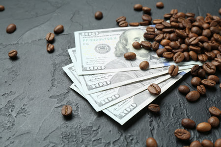 Dollar banknotes and roasted coffee beans on dark textured table, closeup