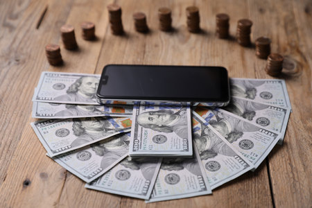 Smartphone, dollar banknotes and coins on wooden tableの写真素材