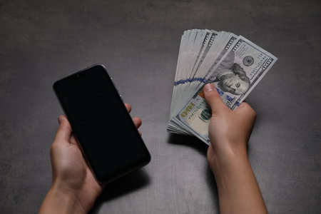 Woman with money and smartphone at grey table, closeupの写真素材
