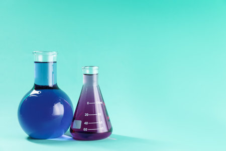 Laboratory glassware with colorful liquids on turquoise background. Space for textの写真素材
