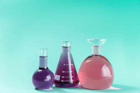 Laboratory glassware with colorful liquids on turquoise background. Space for textの写真素材