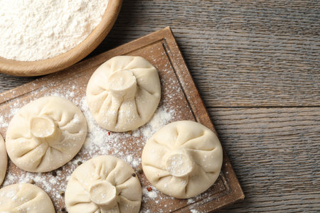 Uncooked khinkalis (dumplings) with peppercorns and flour on wooden table, flat lay. Space for textの写真素材