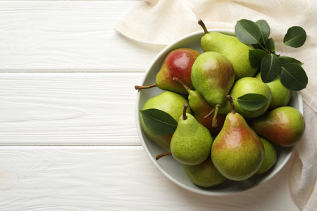 Fresh ripe pears in bowl and green leaves on white wooden table, top view. Space for textの写真素材