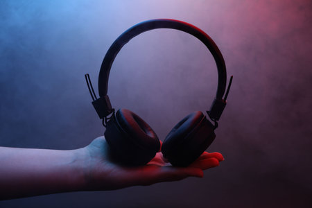 Woman holding wireless headphones on dark background with color lights, closeupの写真素材