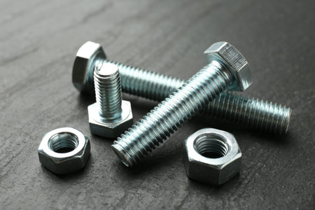 Metal bolts and nuts on black table, closeup