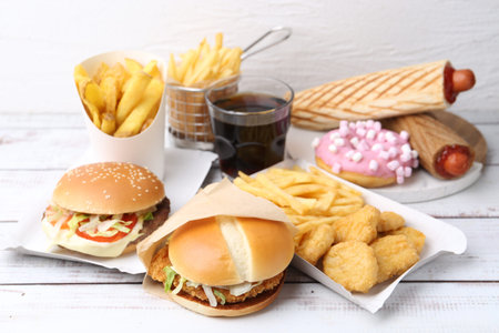 Different delicious fast food and cola on light wooden table, closeupの写真素材
