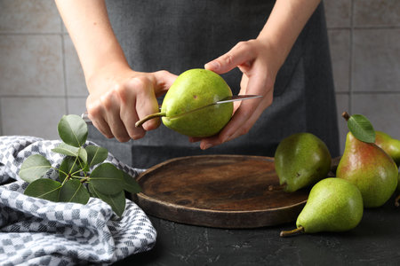 Woman cutting fresh ripe pear at black table, closeupの写真素材