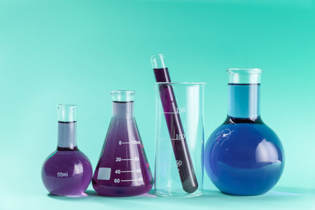 Laboratory glassware with colorful liquids on turquoise background