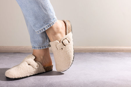 Woman in stylish white slippers on textured floor near grey wall, closeup. Space for text