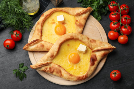 Tasty khachapuri with cheese, egg and other products on black table, flat layの写真素材