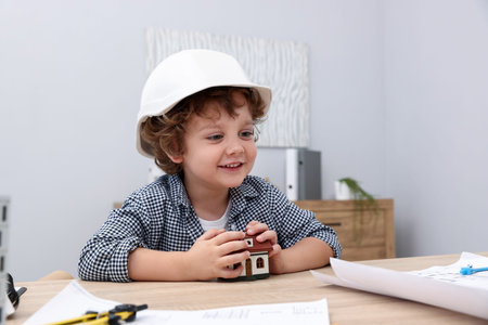 Choice of profession. Little kid in hard hat exploring house model at table indoorsの写真素材