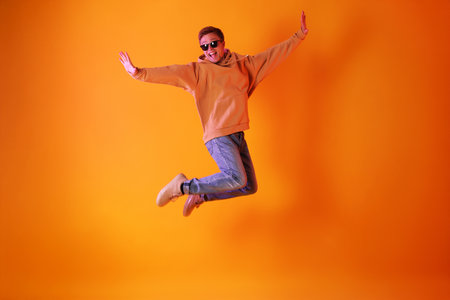 Man wearing sunglasses jumping against orange backgroundの写真素材
