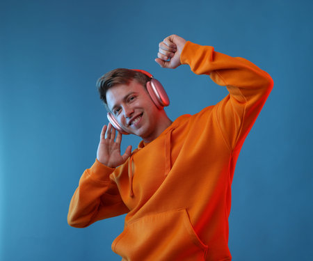 Happy man listening to music in headphones and dancing on blue backgroundの写真素材