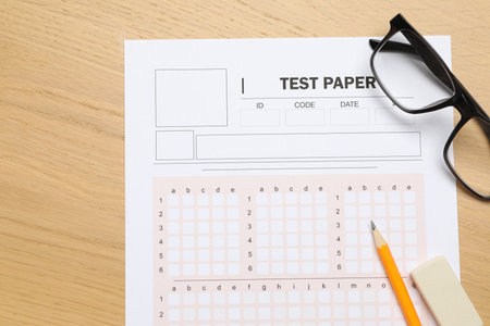 Answer sheet, eraser, pencil and glasses on wooden table, flat lay. Student passing examの写真素材