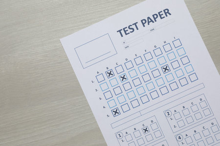 Answer sheet on wooden table, top view. Student passing exam