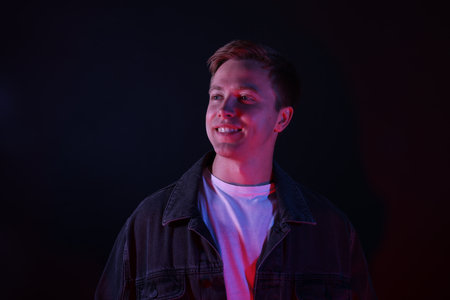 Smiling man in neon lights against black backgroundの写真素材