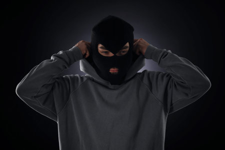 Criminal in mask and hood on dark background
