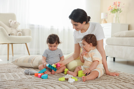 Mother with her cute little twins and toys on floor at home