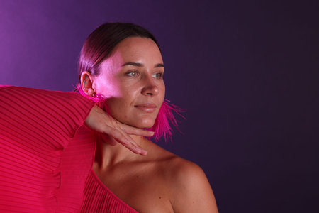 Beautiful woman wearing fur earrings in neon lights against purple background. Space for textの写真素材