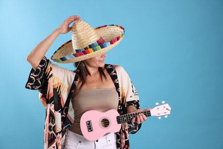 Happy woman in sombrero hat with ukulele on light blue background. Space for textの写真素材