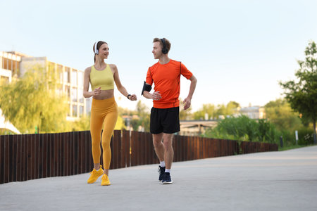 Happy couple in headphones running outdoors, low angle view. Morning exerciseの写真素材