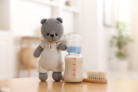 Baby bottle with milk, hair brush and toy bear on table indoorsの写真素材