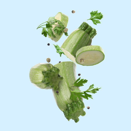 Pieces of fresh zucchinis, parsley and peppercorns falling on light blue backgroundの写真素材