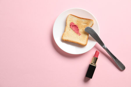 Toast with lipstick and butter knife on light pink background, flat lay. Space for textの写真素材