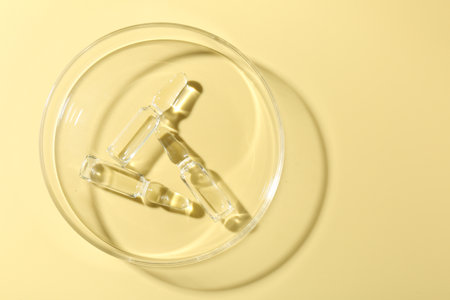 Glass ampoules with liquid and Petri dish on yellow background, top view. Space for textの写真素材