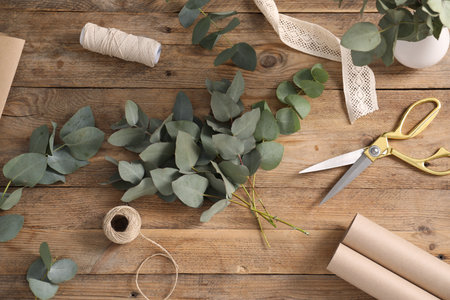 Florist. Eucalyptus branches, threads, ribbon, scissors and wrapping paper on wooden table, flat layの写真素材