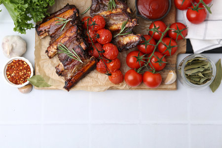 Roasted beef ribs with rosemary, tomatoes and other products on white tiled table, flat lay. Space for textの写真素材