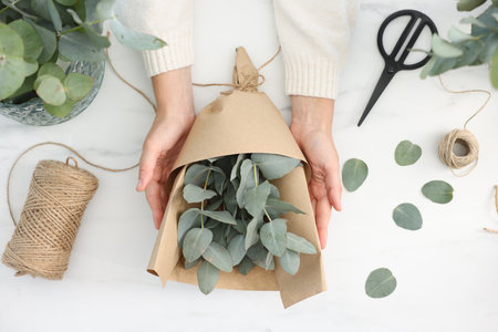 Florist making beautiful bouquet of eucalyptus branches at white marble table, top viewの写真素材
