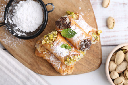 Delicious cannoli with nuts, powdered sugar, chocolate and mint on white wooden table, flat layの写真素材