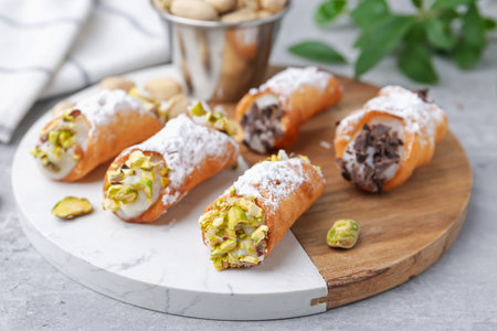 Delicious cannoli with ricotta cheese, pistachios, chocolate and powdered sugar on grey table, closeupの写真素材