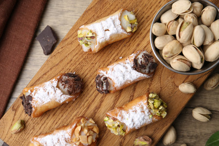 Delicious cannoli with ricotta cheese, peanuts, pistachios, chocolate and powdered sugar on wooden table, flat layの写真素材