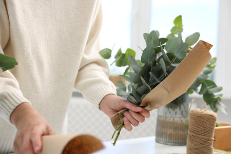 Florist making beautiful bouquet of eucalyptus branches at white table in flower shop, closeupの写真素材