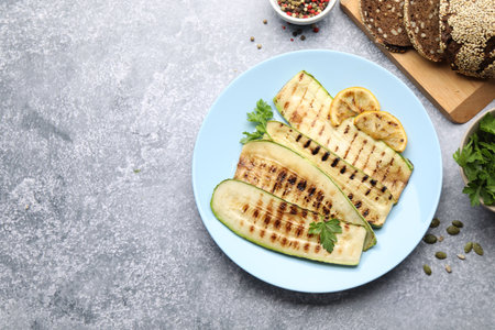 Delicious grilled courgette slices with spices, lemon and bread on gray textured table, flat lay. Space for textの写真素材