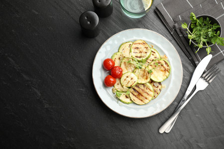 Delicious grilled courgette slices with tomatoes and microgreens served on black textured table, flat lay. Space for textの写真素材