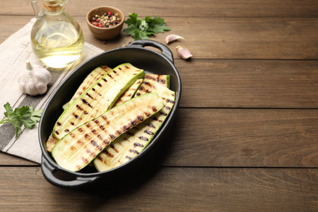 Delicious grilled courgette slices in baking dish, spices and parsley on wooden table, space for textの写真素材