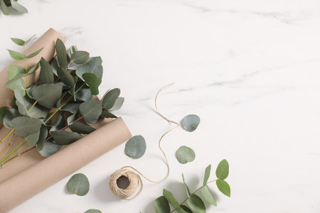 Florist. Eucalyptus branches, thread and wrapping paper on white marble table, flat lay. Space for textの写真素材